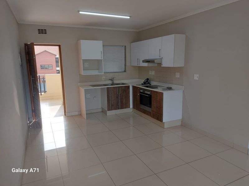 A clean, modern kitchen featuring built-in cabinetry, a stainless steel sink, an integrated oven, and a hob, with neutral tiled flooring throughout.