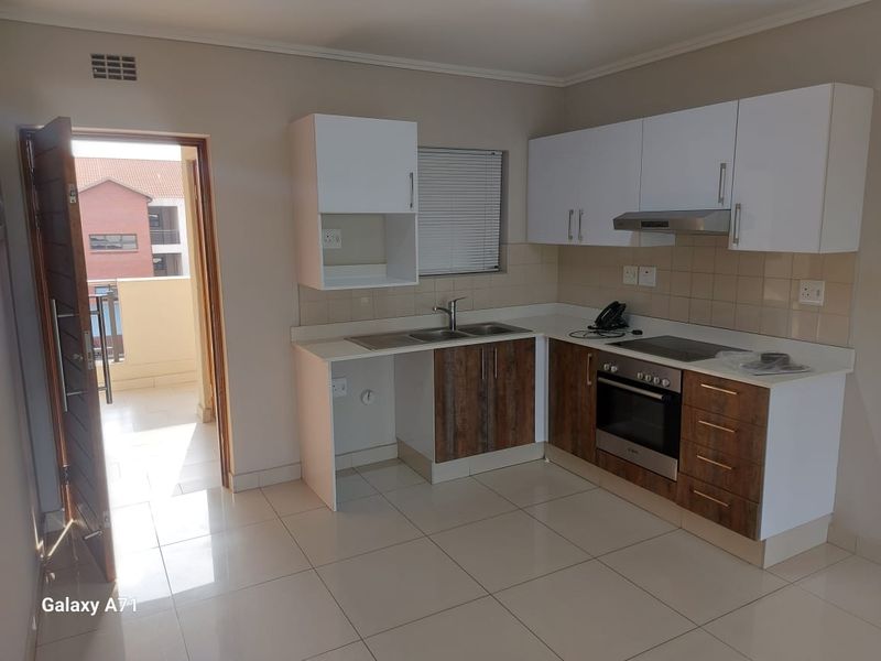 Modern kitchen featuring white and wood-grain cabinetry, built-in oven, hob, extractor fan, and tiled flooring, with direct access to an outdoor balcony.