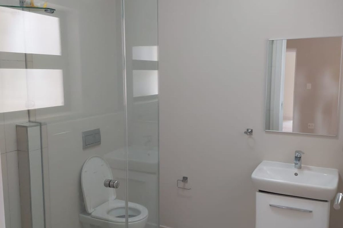A clean, modern bathroom featuring a wall-hung toilet, glass shower enclosure, and a white vanity cabinet with a basin.
