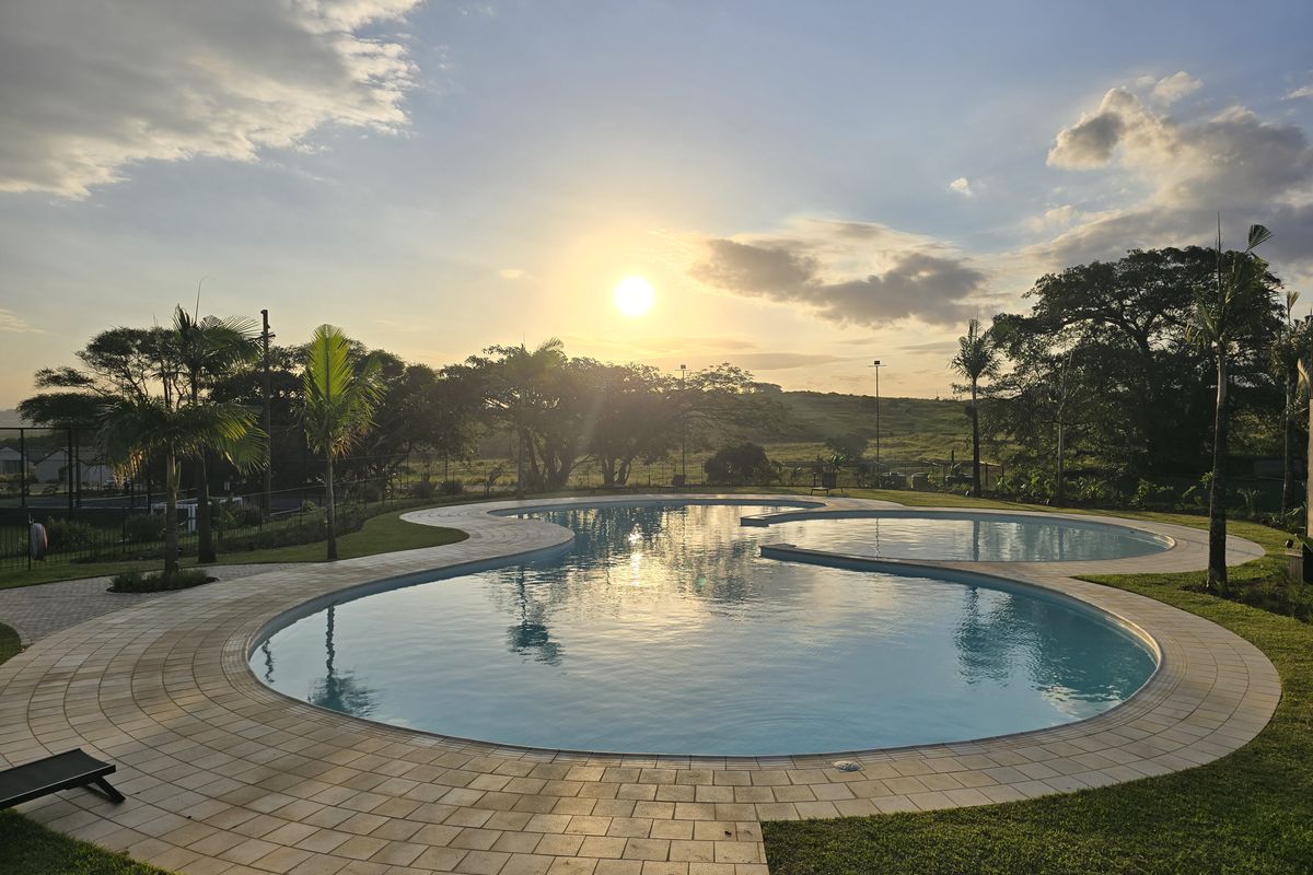 A scenic outdoor swimming pool area featuring a curved design, paved surround, and expansive garden views at sunset.