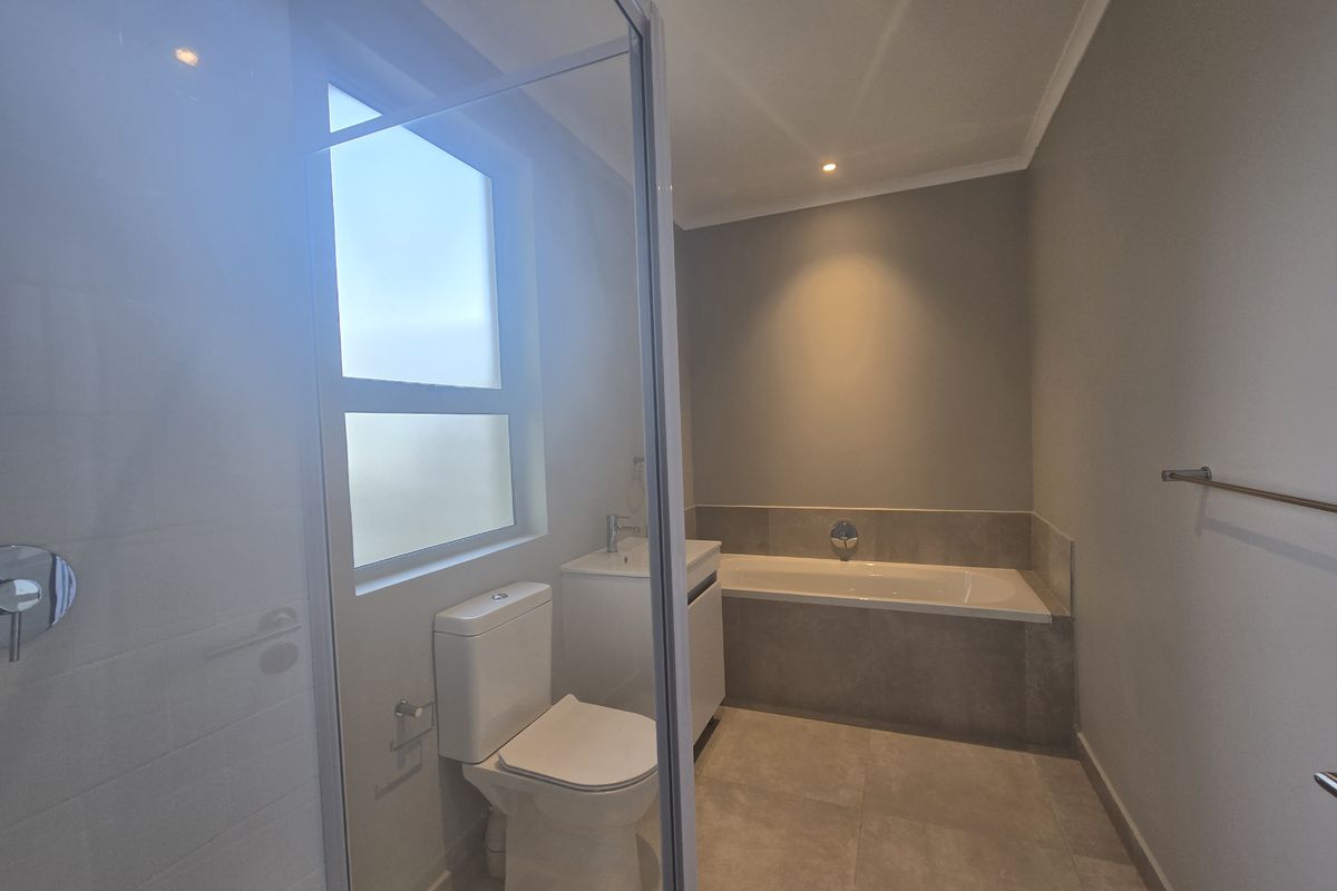 A modern, neutral-toned bathroom featuring a built-in bathtub, a separate glass-enclosed shower, a vanity basin, and a toilet with contemporary floor tiling.