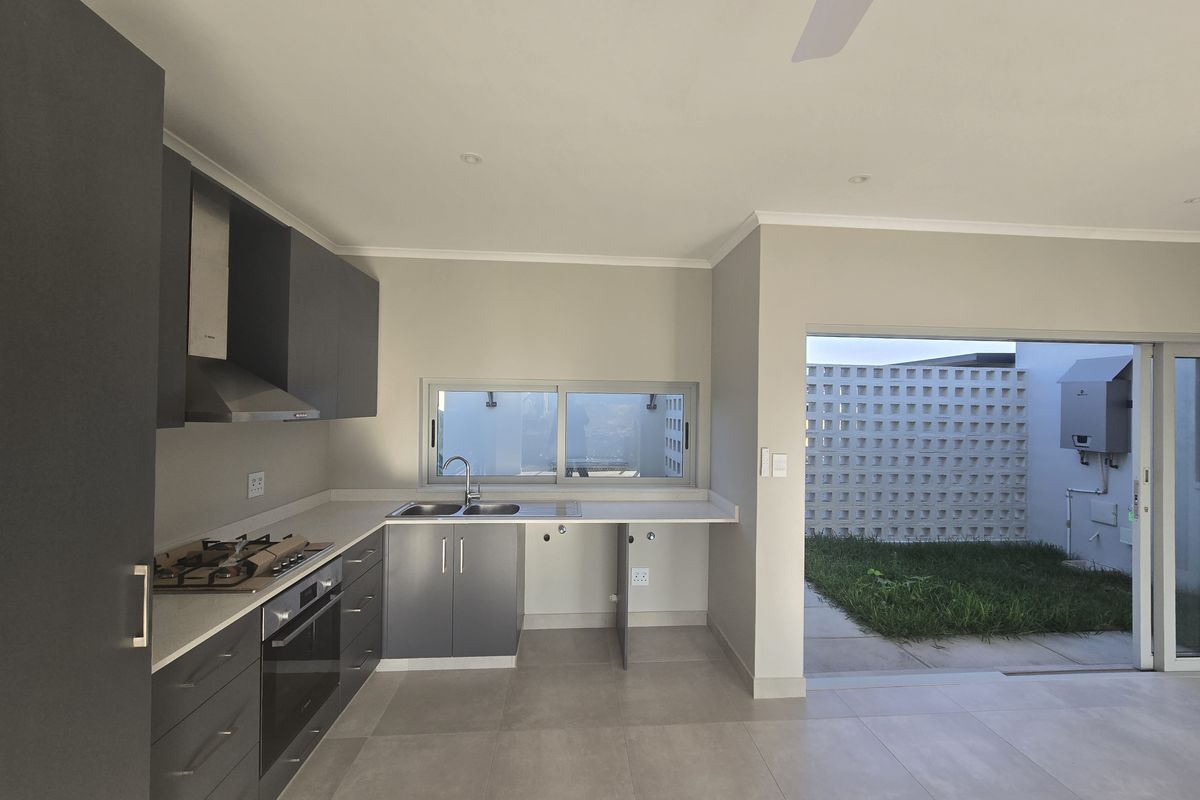 Modern kitchen featuring dark grey cabinetry, built-in oven, gas hob, and direct access to an outdoor patio area through sliding glass doors.
