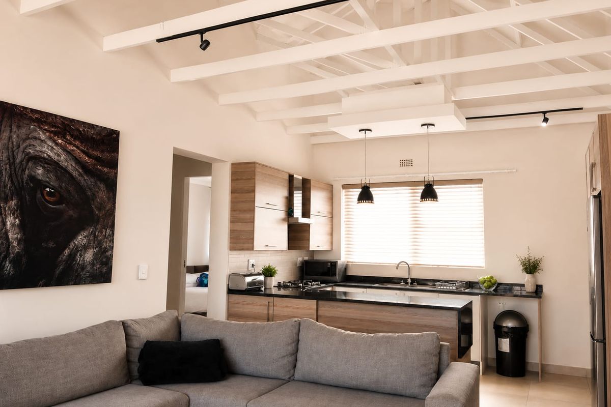 Modern open-plan kitchen and living area featuring exposed white timber beams, sleek laminate cabinetry, granite countertops, and contemporary track lighting.