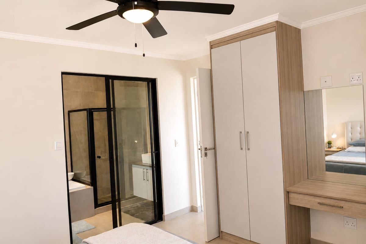 A well-maintained bedroom featuring a built-in wardrobe, integrated vanity, ceiling fan, and an en-suite bathroom with modern glass sliding doors.
