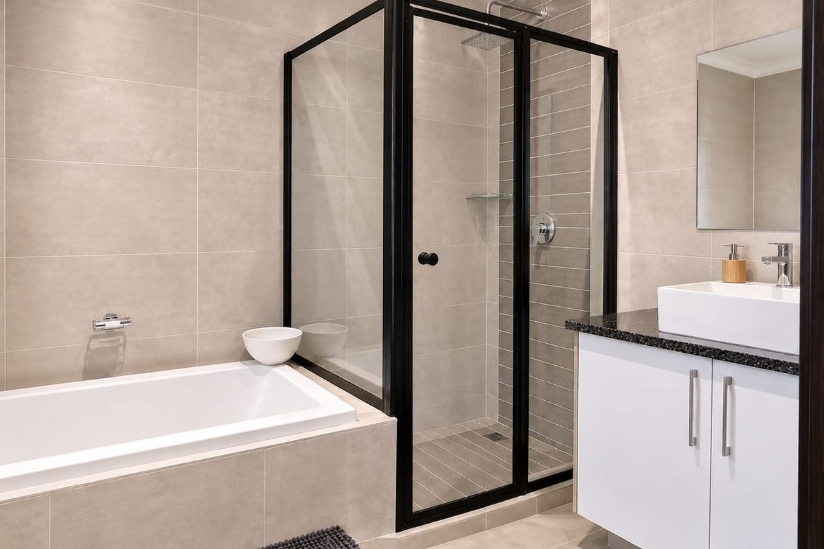 Modern bathroom featuring a built-in bathtub, a walk-in shower with black framing, a vanity cabinet with a countertop basin, and neutral wall tiling.