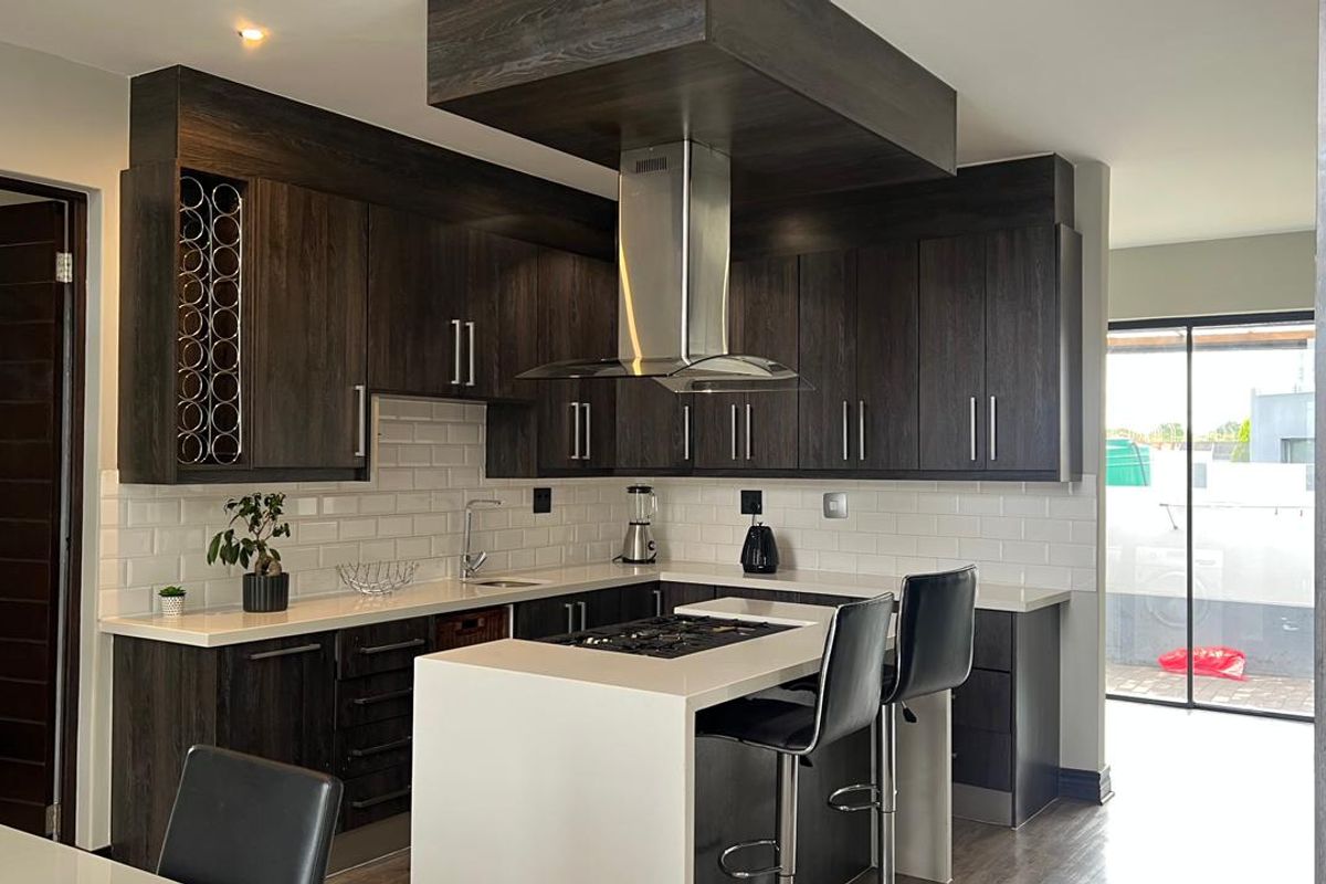 Modern kitchen featuring dark wood cabinetry, white quartz countertops, subway tile backsplash, and a central island with a built-in gas hob.