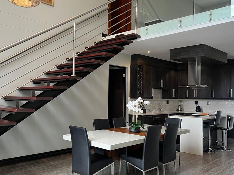 Modern open-plan living area featuring a striking floating staircase with stainless steel balustrades and a contemporary kitchen with dark cabinetry and a central island.