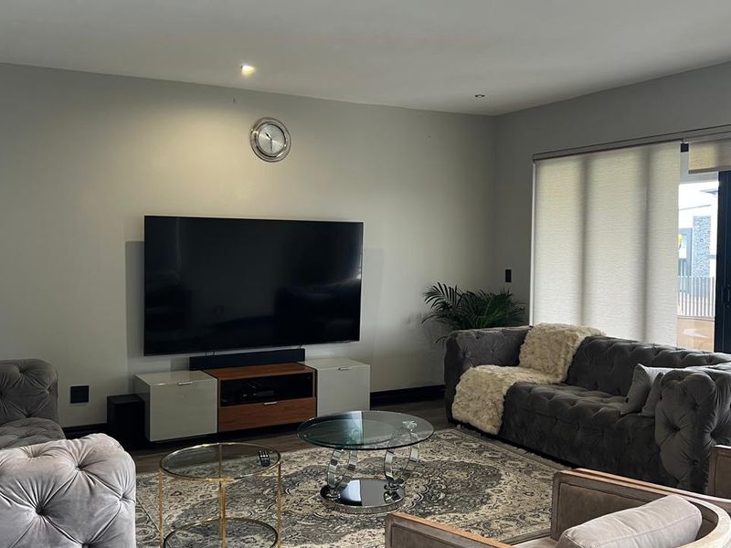 A well-maintained living room featuring recessed downlighting, neutral wall finishes, and large sliding glass doors with roller blinds providing access to the exterior.
