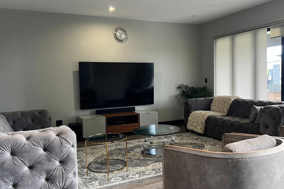 A modern living room featuring recessed downlighting, neutral wall finishes, and large sliding glass doors with roller blinds for natural light control.