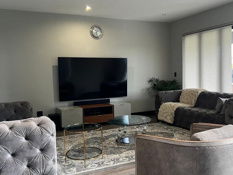 A modern living room featuring recessed downlighting, neutral wall finishes, and large sliding glass doors with roller blinds for natural light control.