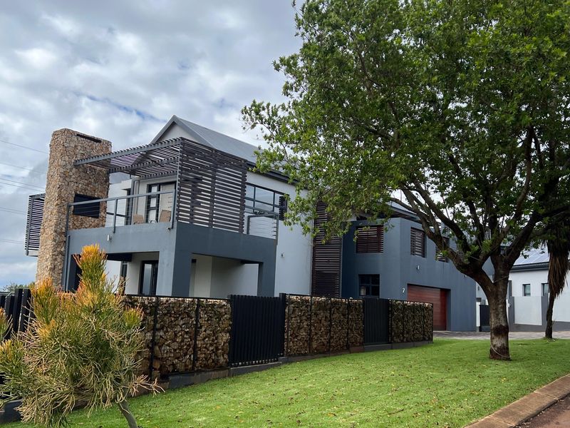 Modern two-story residential property featuring a stone-clad chimney, timber pergola balcony, and contemporary dark grey facade with integrated garage.