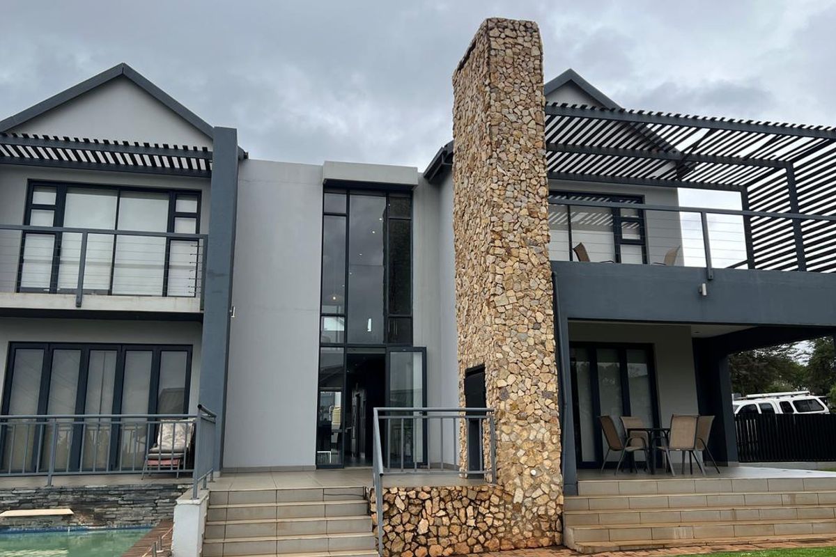 Modern double-story rear elevation featuring a prominent stone-clad chimney, expansive glass sliding doors, and covered patio and balcony areas.
