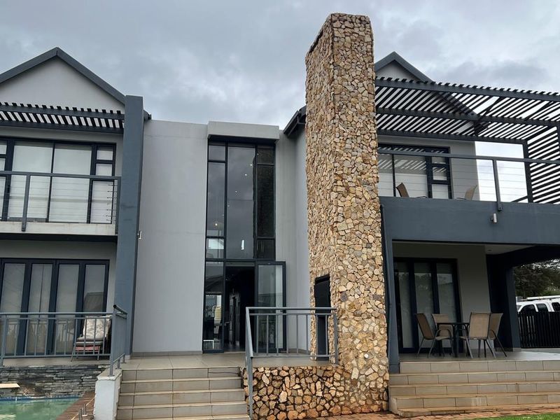 Modern double-story rear elevation featuring a prominent stone-clad chimney, expansive glass sliding doors, and covered patio and balcony areas.