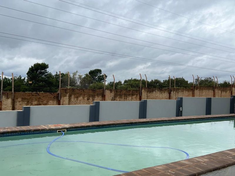 Outdoor swimming pool area featuring a brick boundary wall with electric fencing and tiled pool coping.