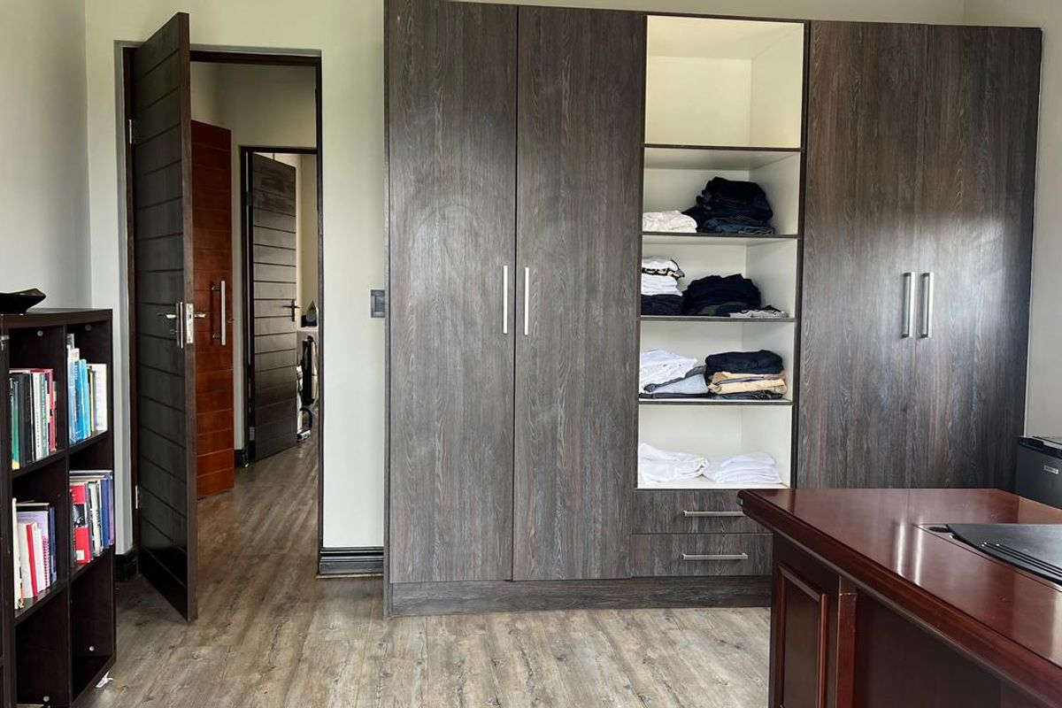 A bedroom featuring dark wood-grain built-in cupboards, laminate flooring, and access to an adjoining hallway.