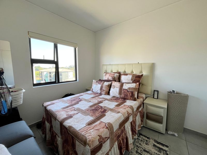 A functional bedroom featuring tiled flooring, a large window with a roller blind, and neutral wall finishes.