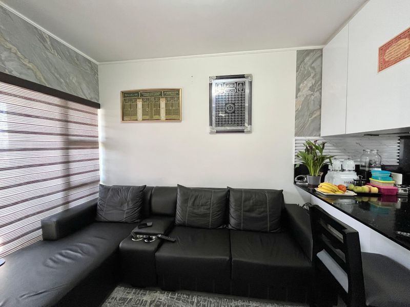 Compact open-plan living area featuring a modern kitchen with black granite countertops, white cabinetry, and marble-effect wall accents.