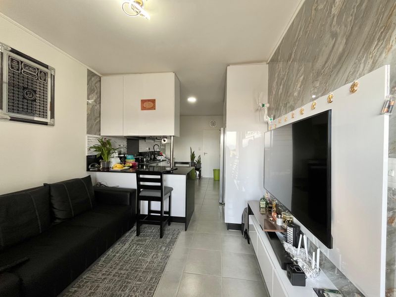 Modern open-plan living area featuring a compact kitchen with breakfast bar, stone-look feature wall, and neutral tiled flooring throughout.