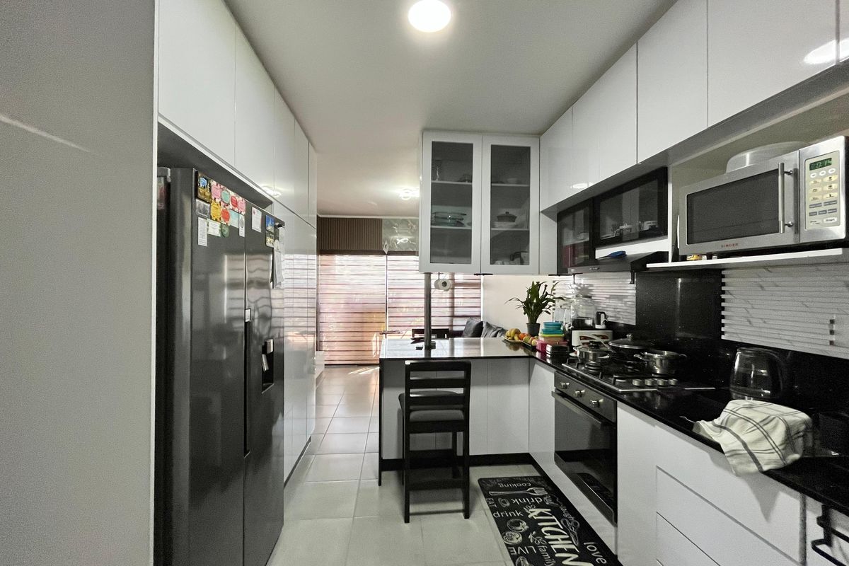 Modern galley-style kitchen featuring white cabinetry, black granite countertops, integrated appliances, and a breakfast bar, leading into an open-plan living area.