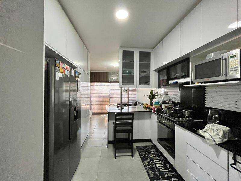 Modern galley-style kitchen featuring white cabinetry, black granite countertops, integrated appliances, and a breakfast bar, leading into an open-plan living area.
