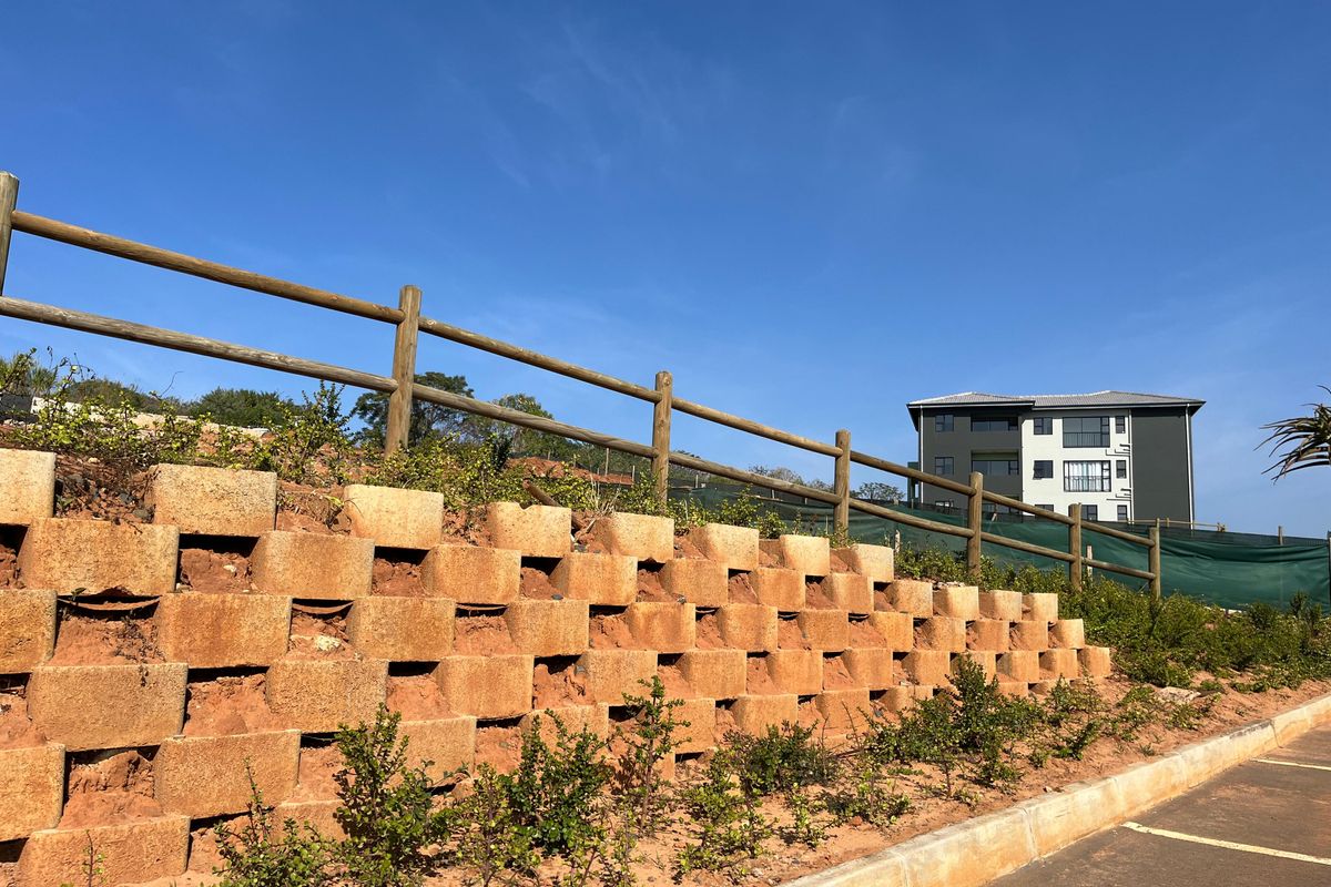 Exterior view of a tiered retaining wall with timber fencing, adjacent to a paved parking area and apartment building.