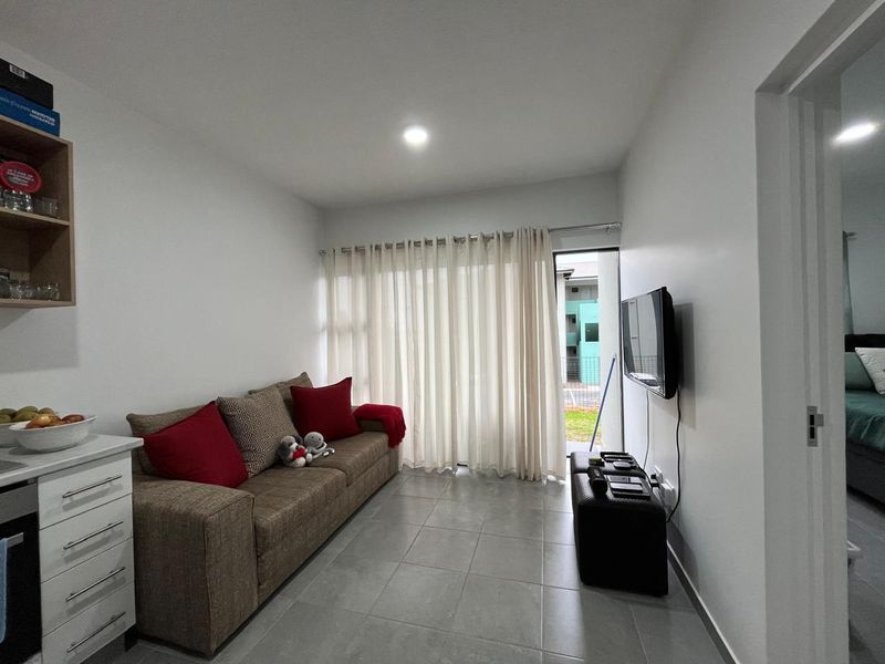 A bright living room featuring neutral tiled flooring, recessed ceiling lighting, and a sliding glass door providing access to the exterior.