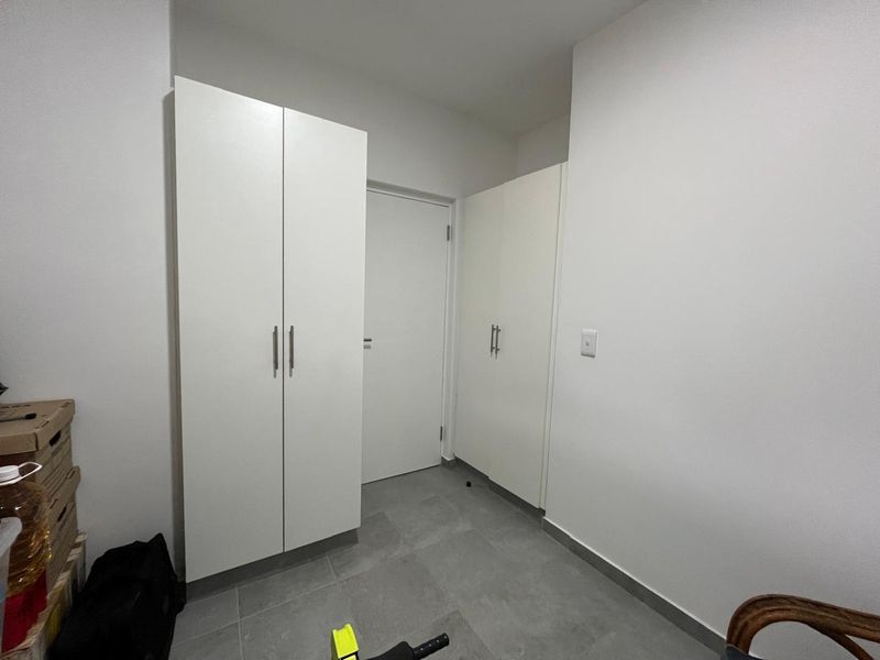 A clean, minimalist hallway featuring neutral tiled flooring and ample built-in cupboard storage with modern white finishes.