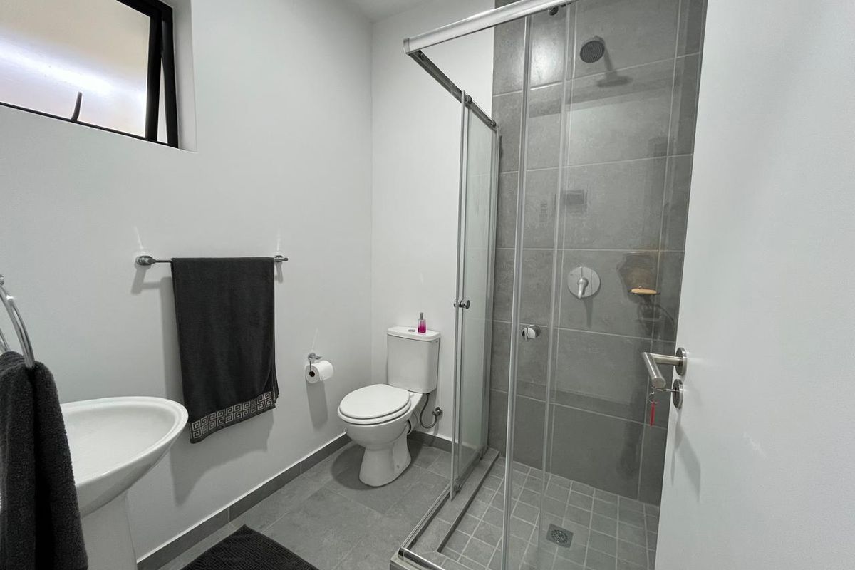 A modern, clean bathroom featuring a pedestal sink, a toilet, and a glass-enclosed shower with grey tiled finishes.