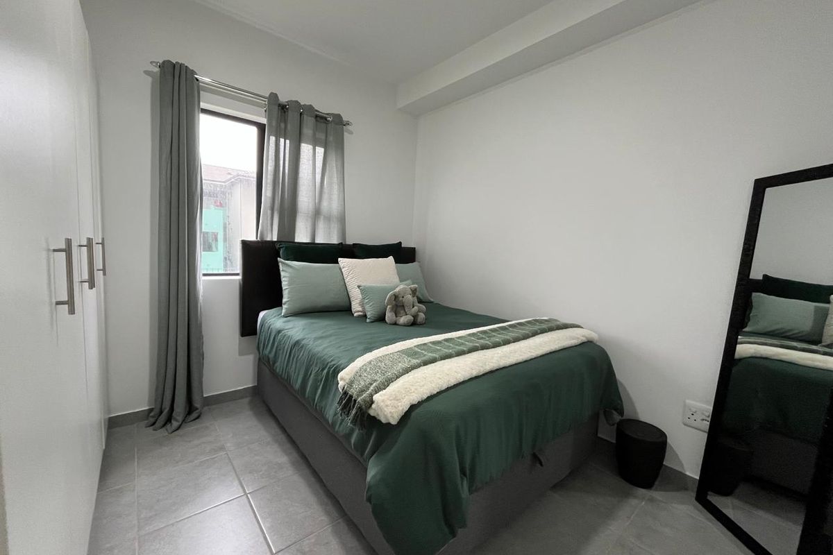 A compact, well-maintained bedroom featuring neutral tiled flooring, a built-in wardrobe, and a window providing natural light.
