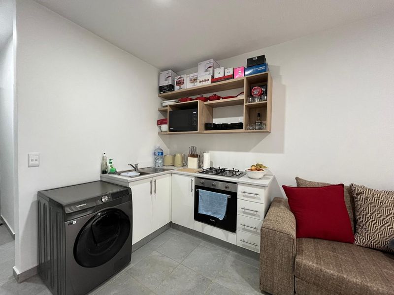 Compact open-plan kitchen area featuring white cabinetry, gas hob, built-in oven, and integrated laundry space, finished with modern tiled flooring.
