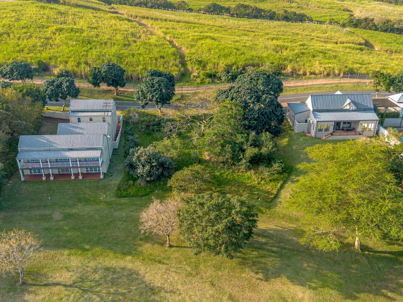Aerial view of a residential property featuring multiple buildings, expansive green lawns, mature trees, and surrounding agricultural landscape.