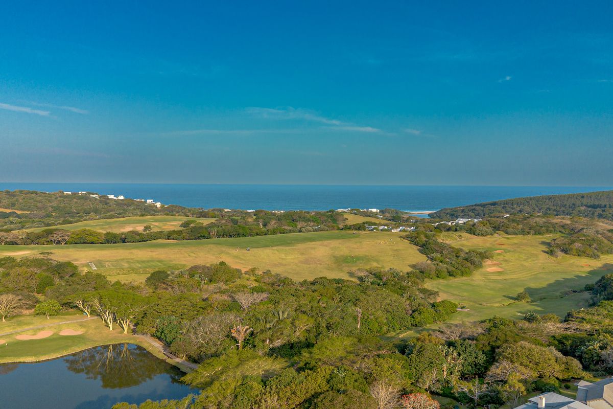 An expansive aerial view of a coastal golf course estate featuring lush green fairways, natural vegetation, and a scenic ocean backdrop.