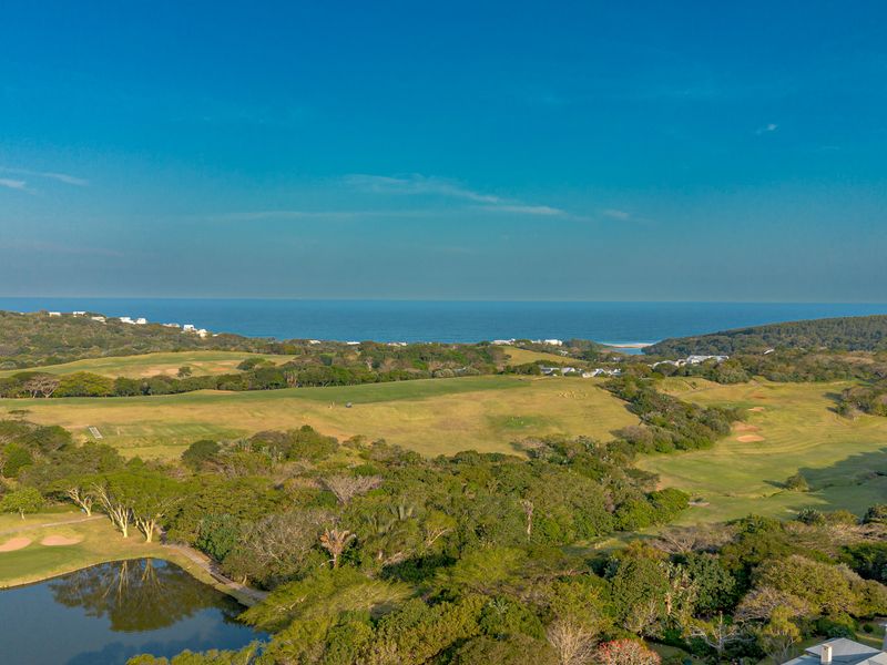 An expansive aerial view of a coastal golf course estate featuring lush green fairways, natural vegetation, and a scenic ocean backdrop.