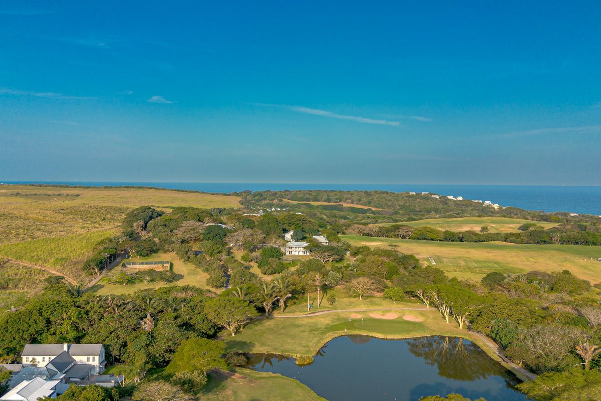 An aerial view of a coastal residential estate featuring lush green landscapes, a golf course, and a scenic water feature overlooking the ocean.