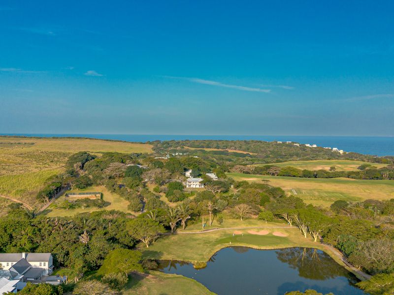 An aerial view of a coastal residential estate featuring lush green landscapes, a golf course, and a scenic water feature overlooking the ocean.