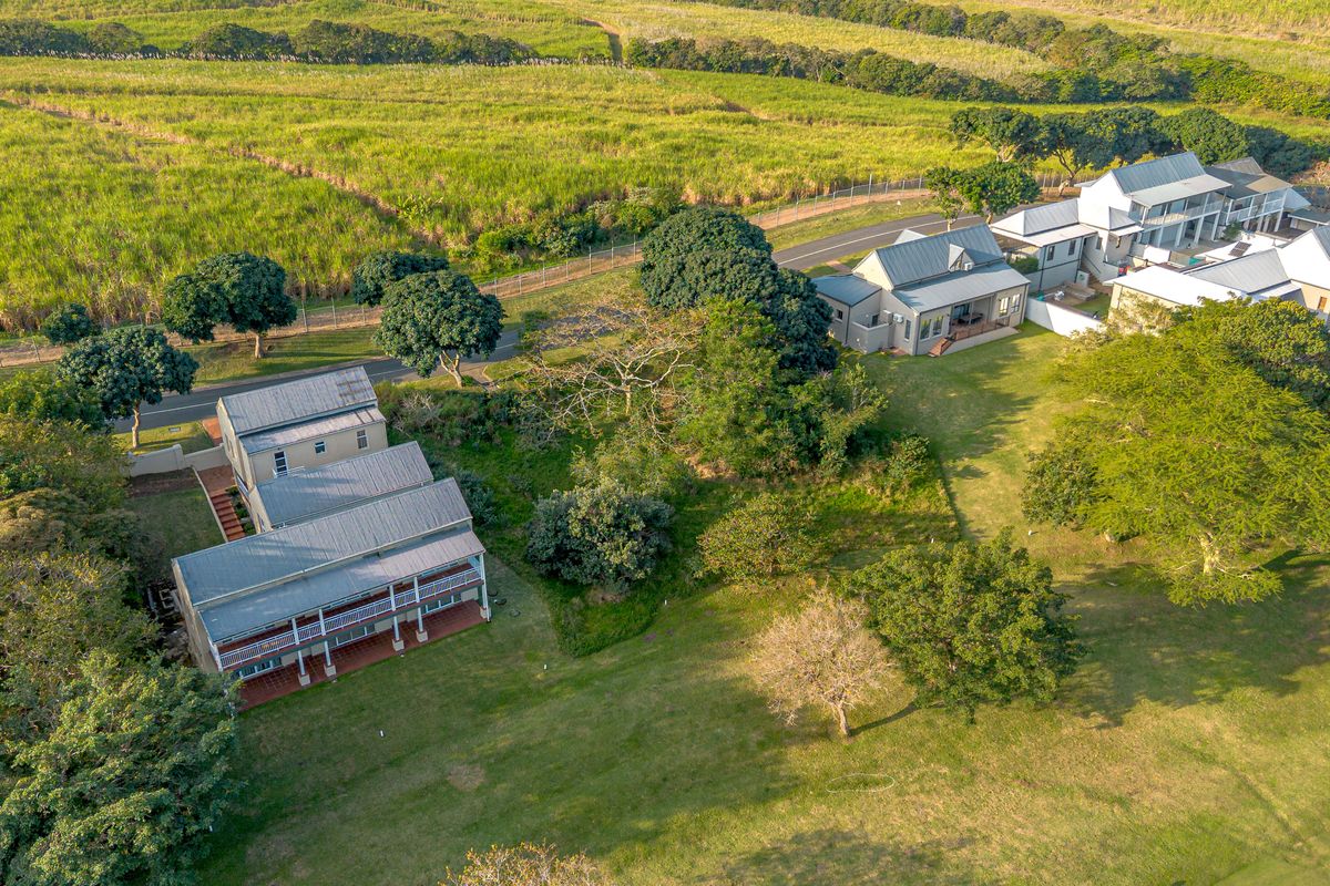Aerial view of a residential estate featuring multiple multi-level homes, expansive green lawns, mature trees, and paved access paths within a rural landscape.