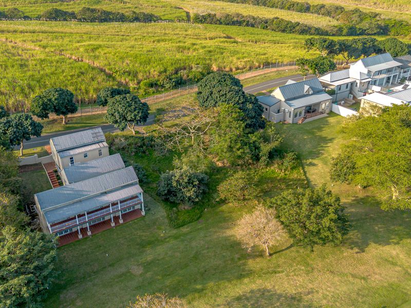 Aerial view of a residential estate featuring multiple multi-level homes, expansive green lawns, mature trees, and paved access paths within a rural landscape.