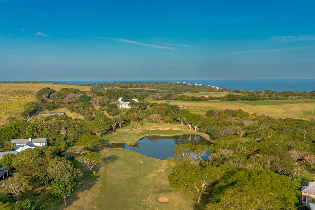 An aerial view of a residential estate featuring a golf course, a central water hazard, and surrounding coastal landscape.
