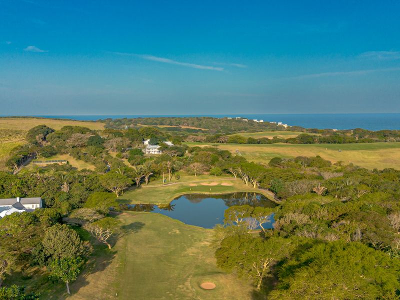 An aerial view of a residential estate featuring a golf course, a central water hazard, and surrounding coastal landscape.