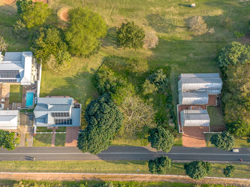 Aerial view of residential properties featuring metal roofs, solar panels, swimming pools, and landscaped gardens situated along a road.