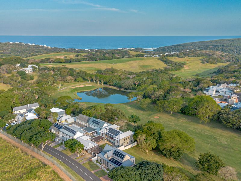 Aerial view of a residential estate featuring modern homes with solar panels, situated adjacent to a golf course, lake, and coastal landscape.
