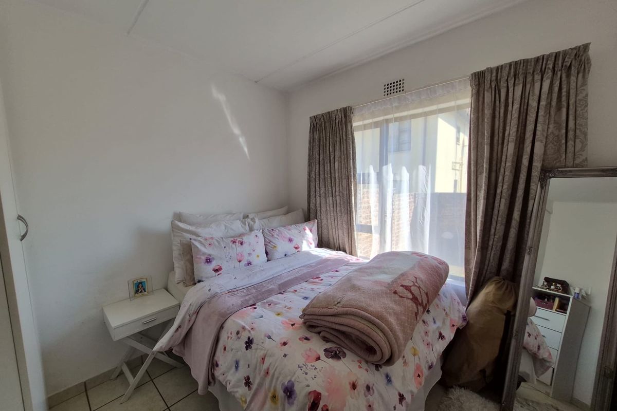 A functional bedroom featuring tiled flooring, a built-in cupboard, and a window with curtain tracks, providing a comfortable living space.