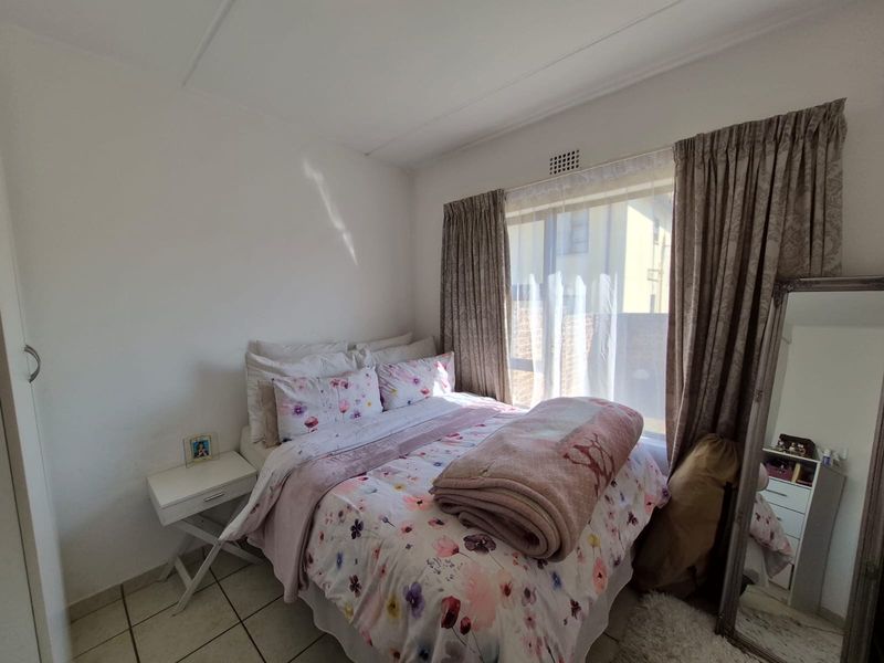 A functional bedroom featuring tiled flooring, a built-in cupboard, and a window with curtain tracks, providing a comfortable living space.