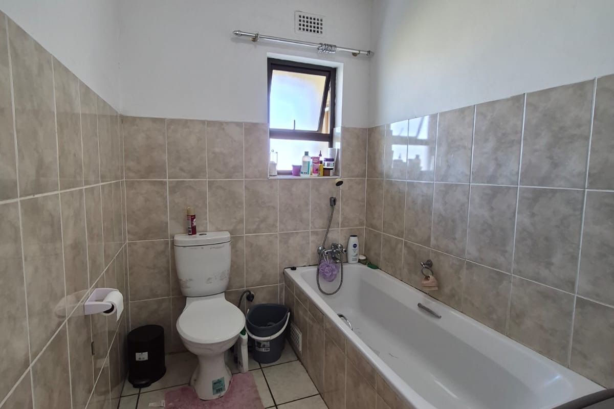 A functional bathroom featuring neutral ceramic wall and floor tiles, a standard bathtub, and a toilet, offering a clean and practical layout.