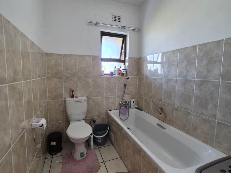 A functional bathroom featuring neutral ceramic wall and floor tiles, a standard bathtub, and a toilet, offering a clean and practical layout.