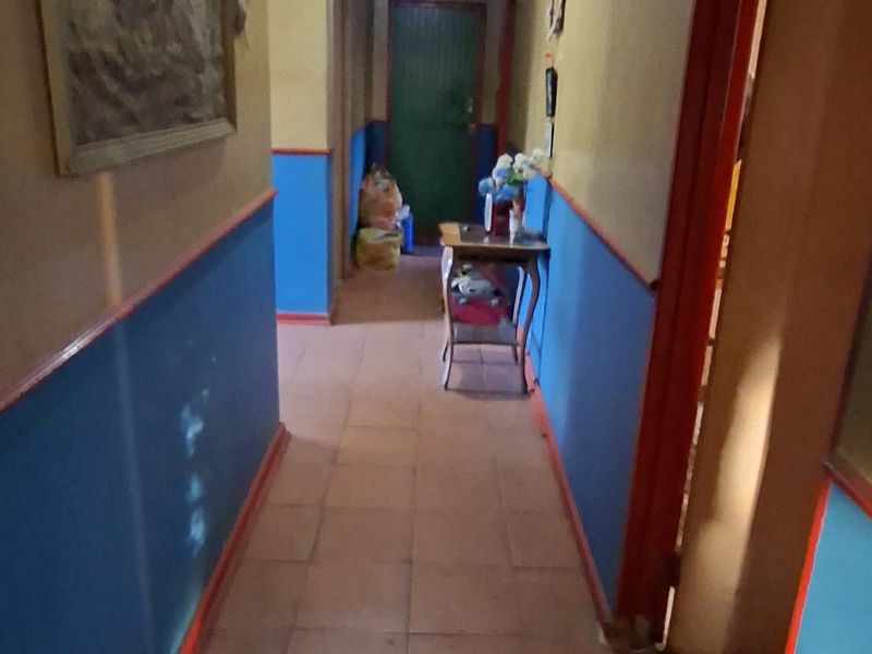 A narrow residential hallway featuring tiled flooring and dated wall finishes, providing access to multiple rooms within the home.