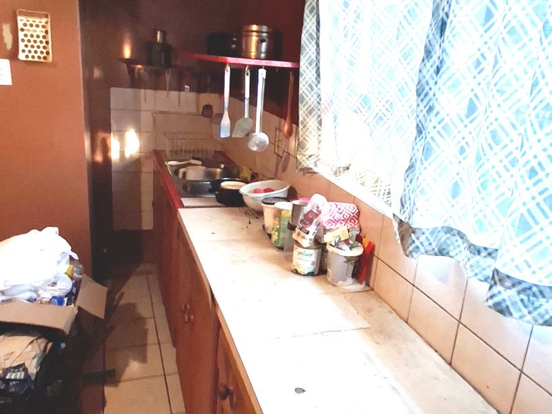 A dated kitchen featuring wooden cabinetry, tiled backsplash, and tiled flooring, offering a functional layout in need of modernization.