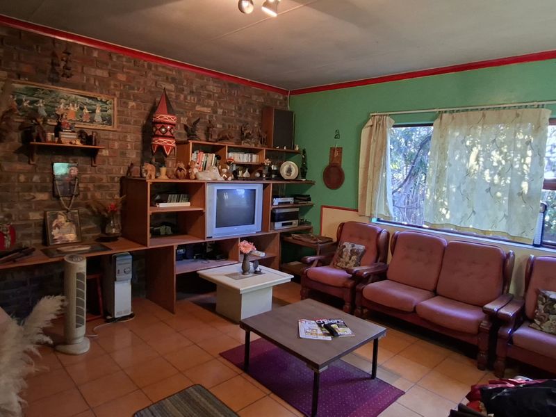 A living room featuring an exposed brick wall, tiled flooring, and a built-in shelving unit, offering potential for modernization and aesthetic updates.