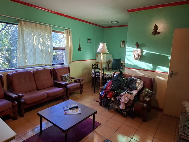 A living room featuring tiled flooring and a large window, currently requiring cosmetic updates to modernize the dated wall finishes and overall aesthetic.