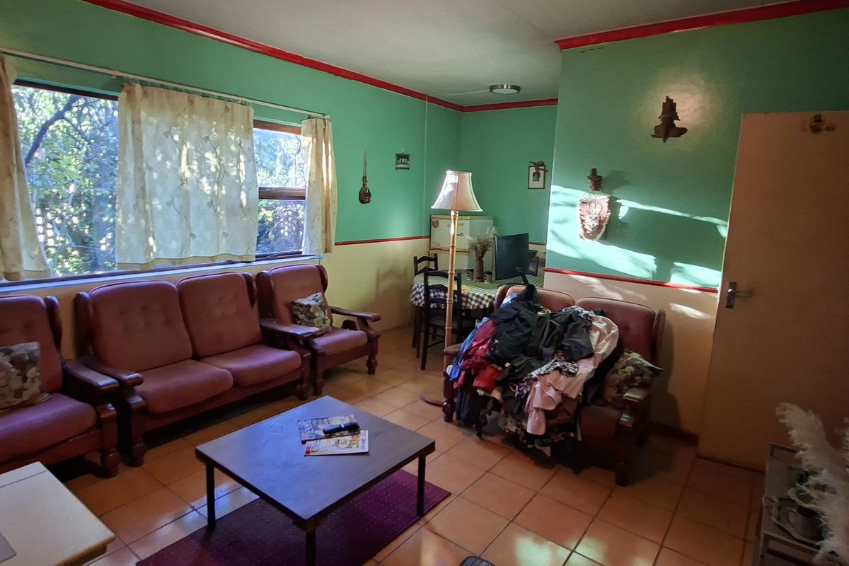 A living room featuring tiled flooring and a large window, currently requiring cosmetic updates to modernize the dated wall finishes and overall aesthetic.